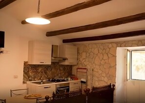 Eine Küche mit Steinwand, Holzbalken, einem Herd und einem Esstisch mit Stühlen.