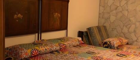 A bed with a colorful quilt, a wooden headboard, and a stone wall.