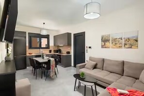 Ein modernes Wohnzimmer mit einer Couch, einem Esstisch mit Stühlen, einem kleinen Couchtisch und einer Küche im Hintergrund.