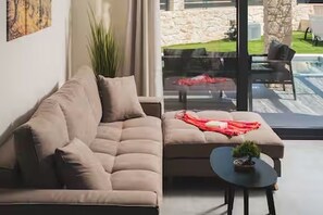 Ein modernes Wohnzimmer mit einer Couch, einem kleinen Tisch mit Pflanze und Blick auf eine Steinmauer und einen Außenbereich durch eine Glastür.
