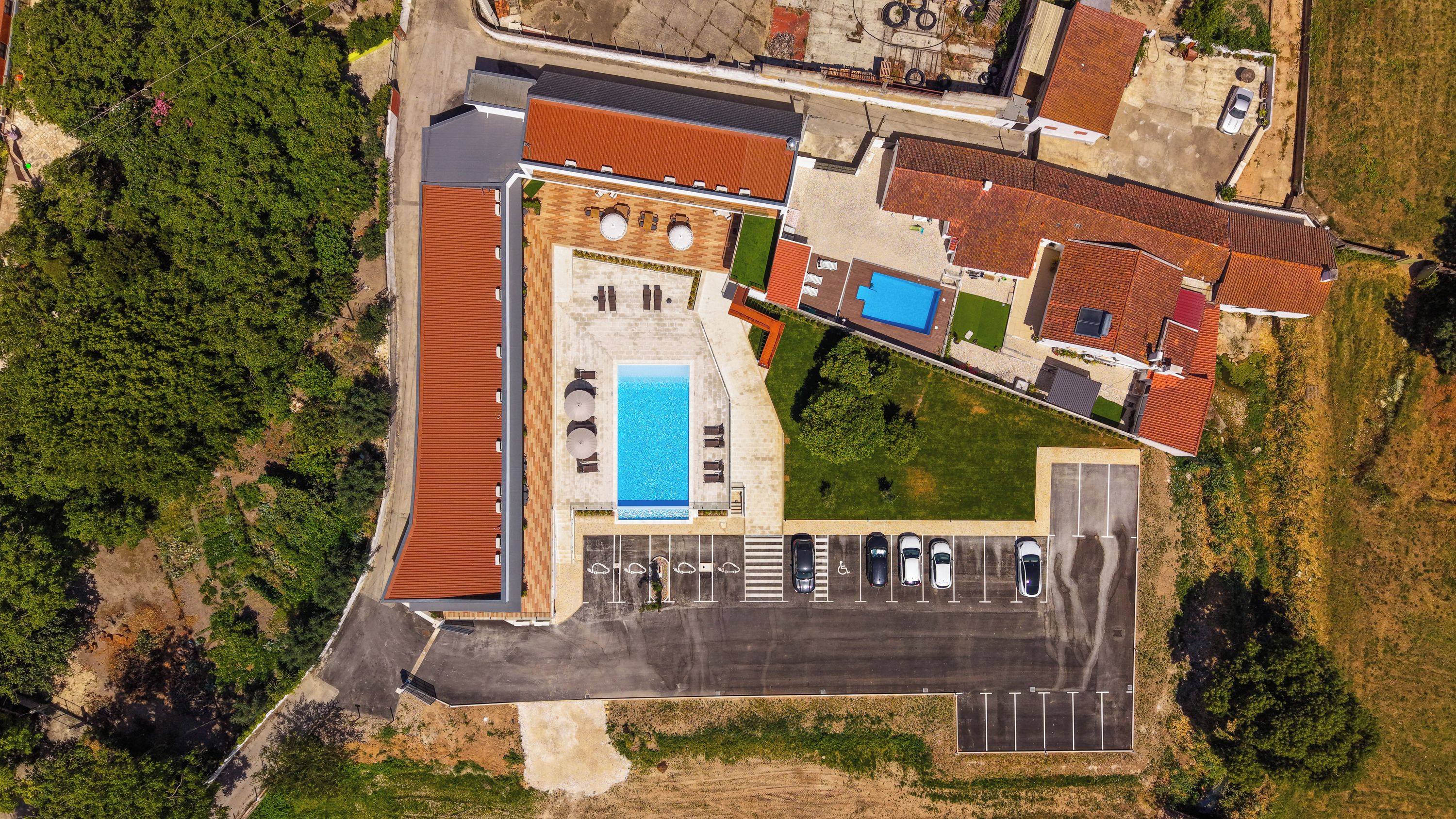 An aerial view of a property with a swimming pool, multiple parking spaces, and a large open area.