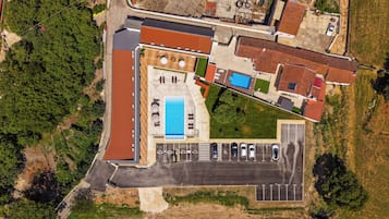 An aerial view of a property with a swimming pool, multiple parking spaces, and a large open area.