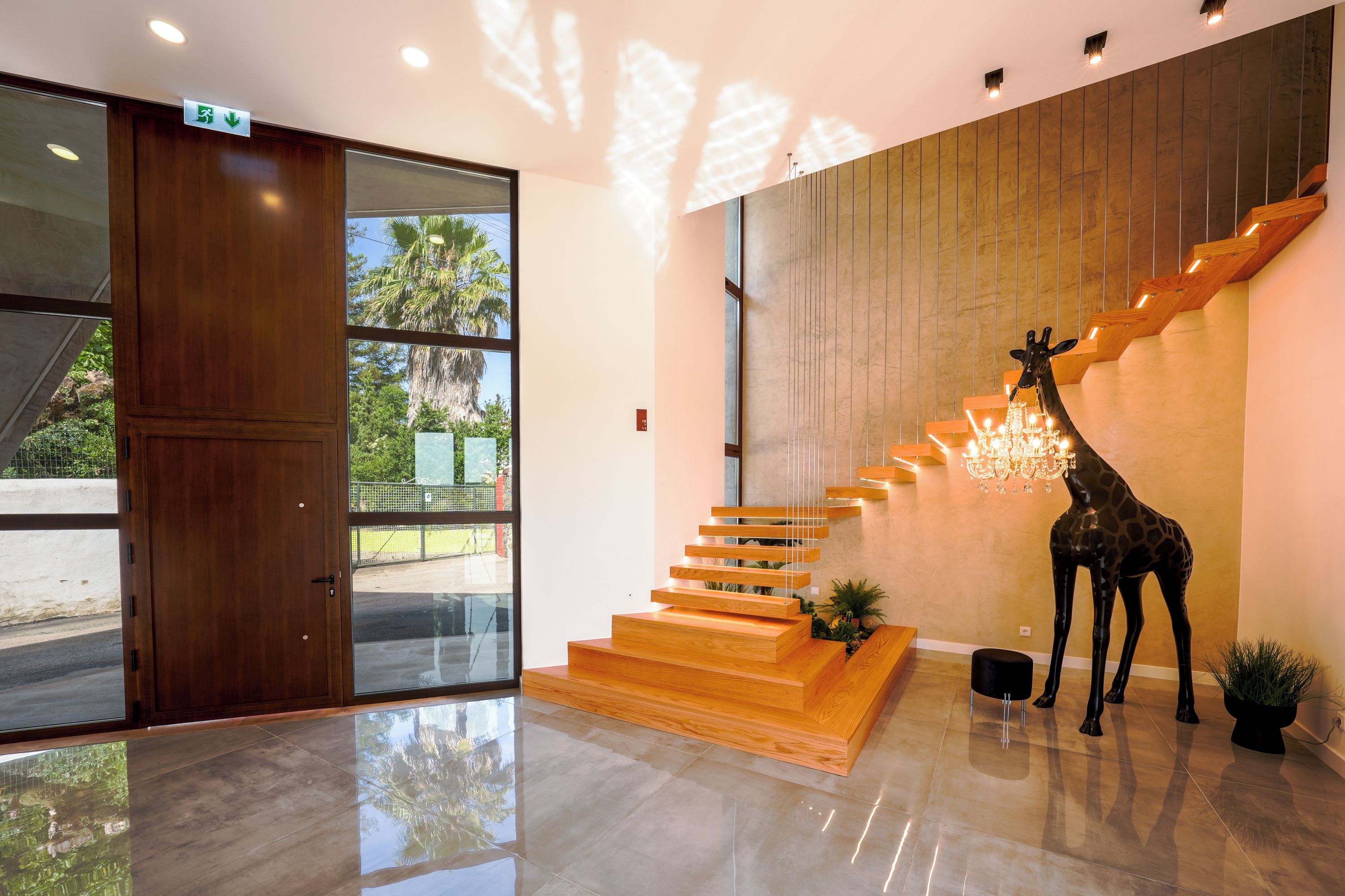 Un interior moderno con una escalera de madera, una escultura de jirafa y una puerta de cristal que da al exterior.