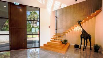Interior moderno com escada de madeira, escultura de girafa e porta de vidro que dá para o exterior.
