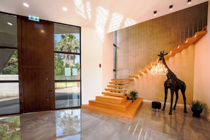 A modern interior with a wooden staircase, a giraffe sculpture, and a glass door leading outside.