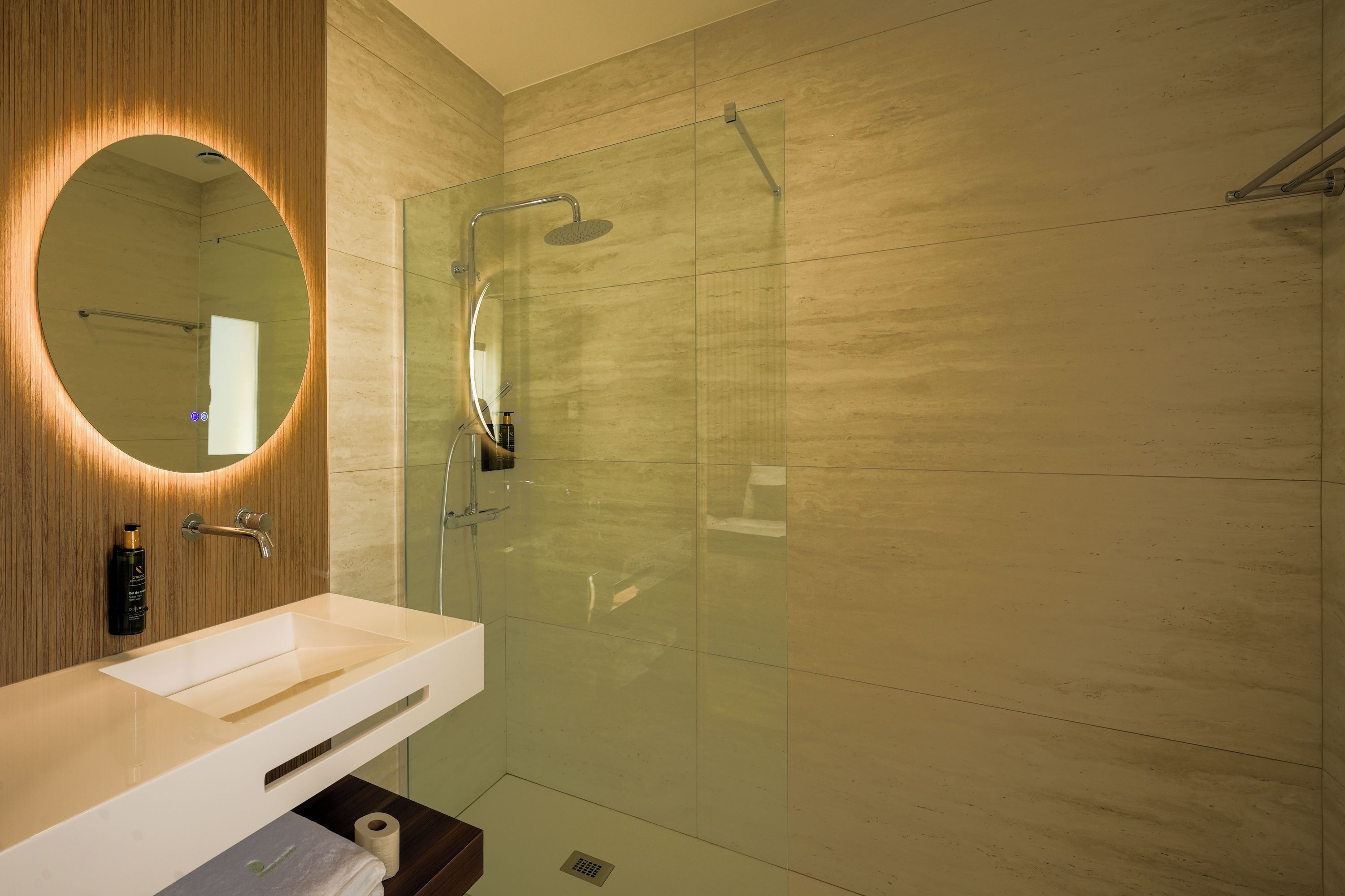 A modern bathroom with a glass shower enclosure, a round mirror, and a white sink.