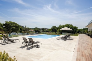 A swimming pool with lounge chairs and an umbrella, surrounded by a paved patio and greenery.