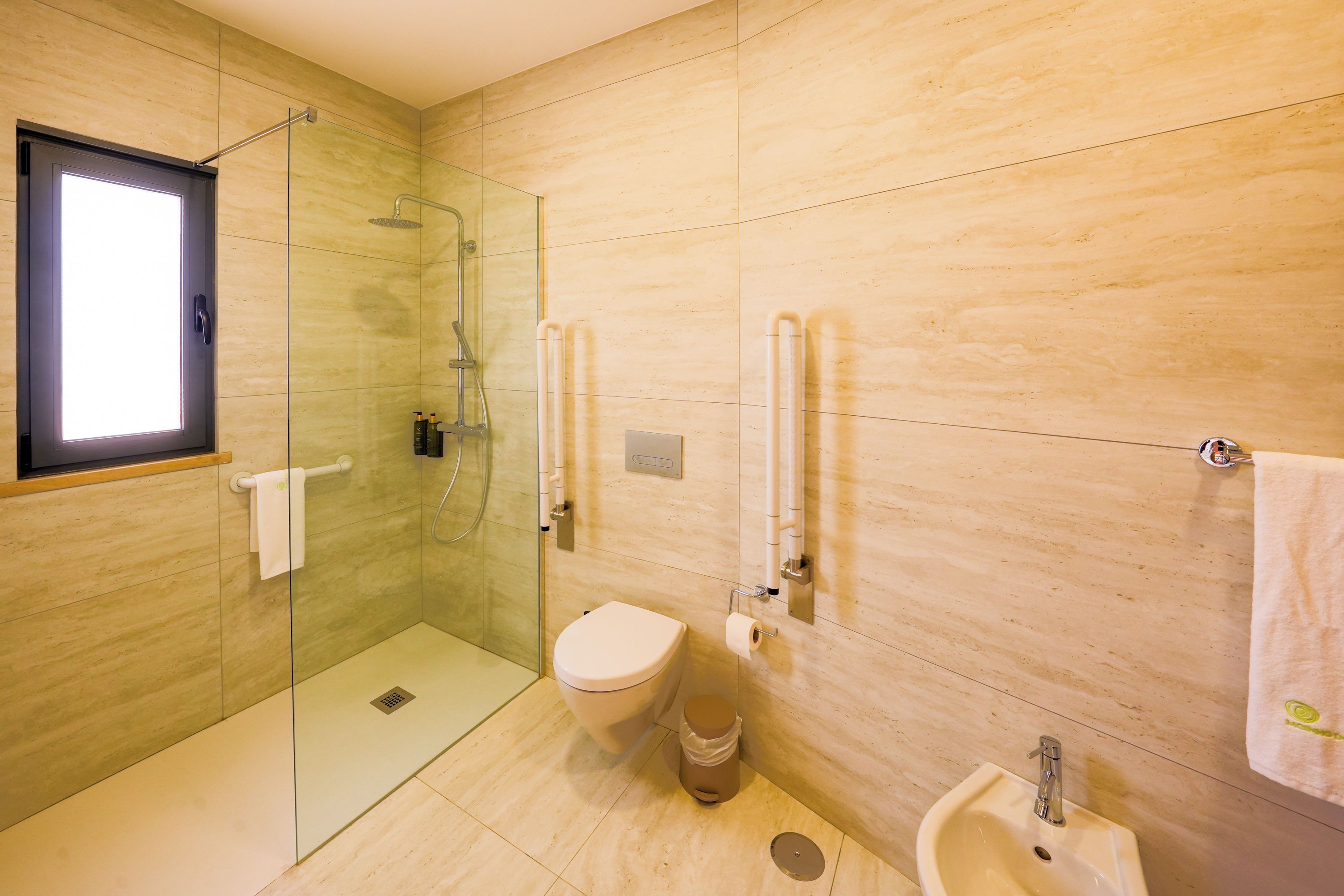 A modern bathroom with a glass shower enclosure, a toilet, a sink, and a towel rack.