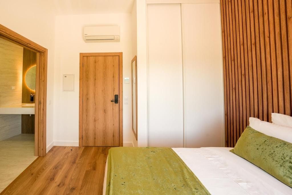 Un dormitorio con una puerta de madera, una cama con ropa de cama verde y un armario blanco.
