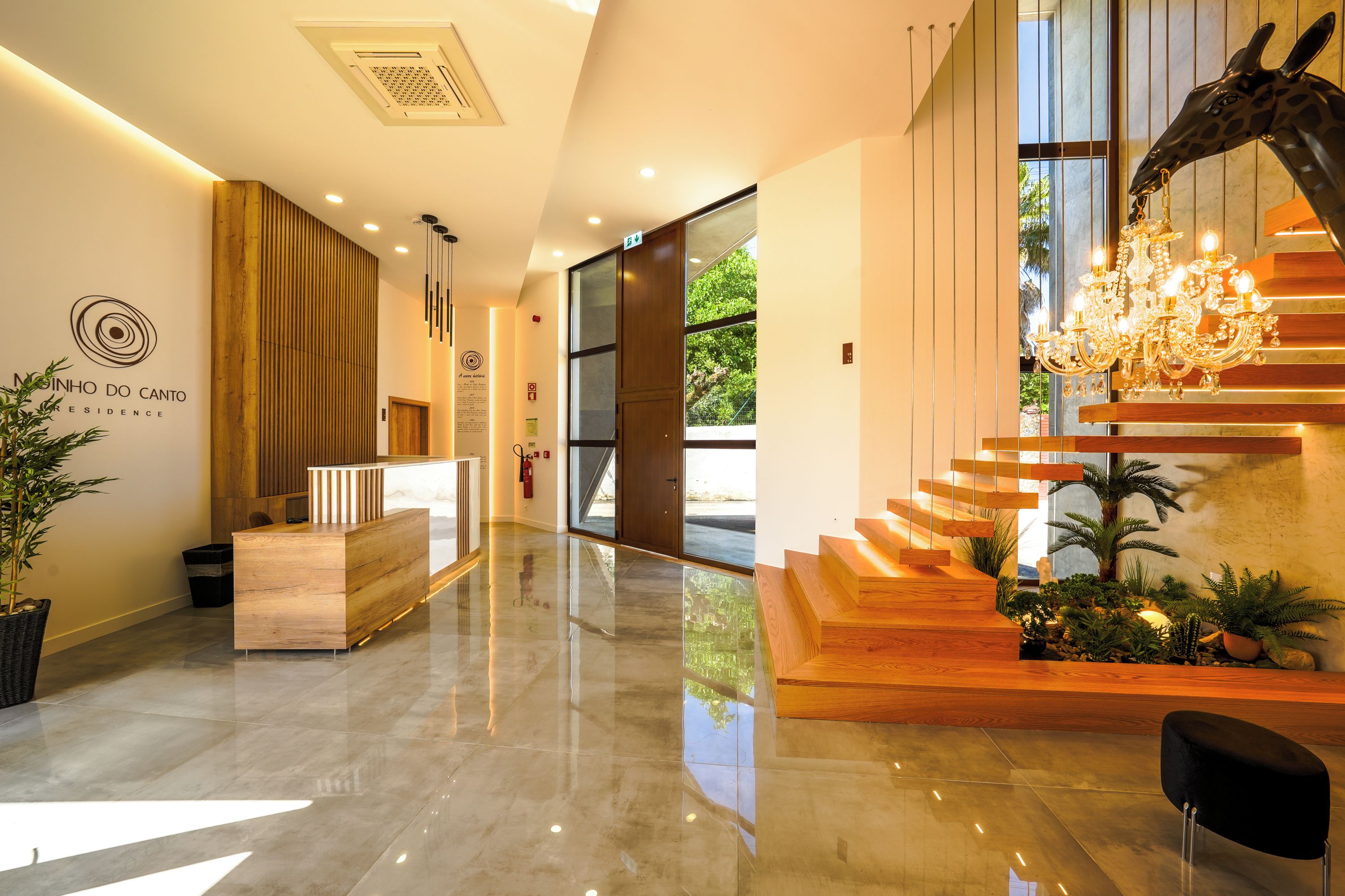 Um saguão moderno de hotel com balcão de recepção, escada com escultura de girafa e lustre.