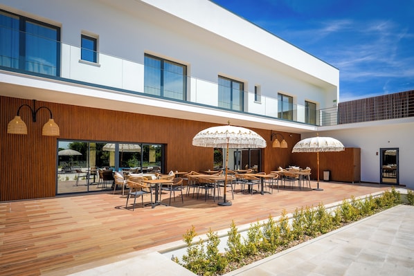 A modern outdoor seating area with wooden flooring, tables, and umbrellas.
