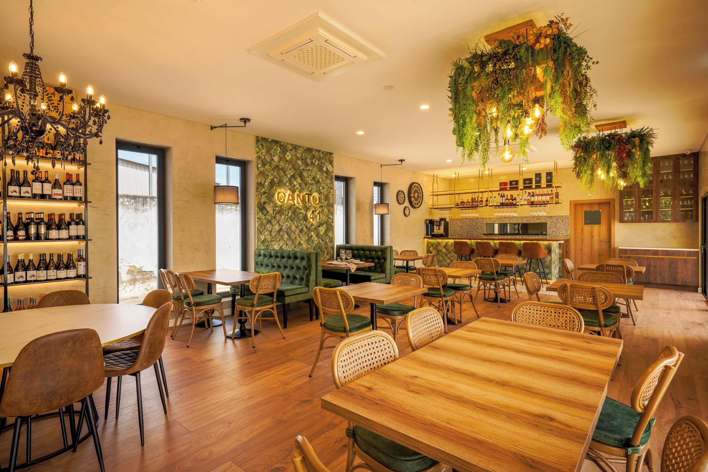 Un interior de restaurante con mesas y sillas de madera, una zona de bar y un área de asientos con cojines verdes.