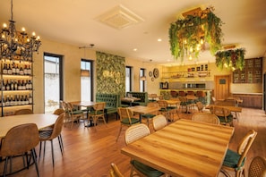 Un interior de restaurante con mesas y sillas de madera, una zona de bar y un área de asientos con cojines verdes.