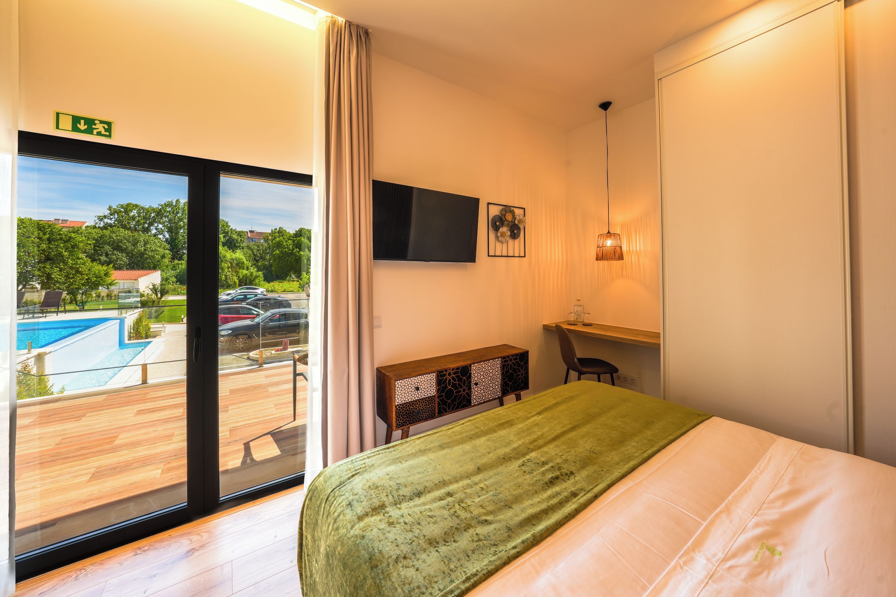 Habitació d'hotel amb un llit, una taula de nit, una televisió i vista a una piscina.