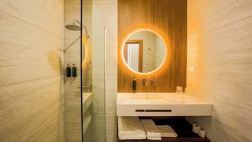 A modern bathroom with a glass-enclosed shower, a wooden vanity with a built-in sink, and a mirror with a circular light.