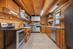 A compact kitchen with wooden cabinets, stainless steel appliances, and a patterned floor. - Chalet de Réception Domaine de l'Archipel (Sainte-Anne-de-Sorel)