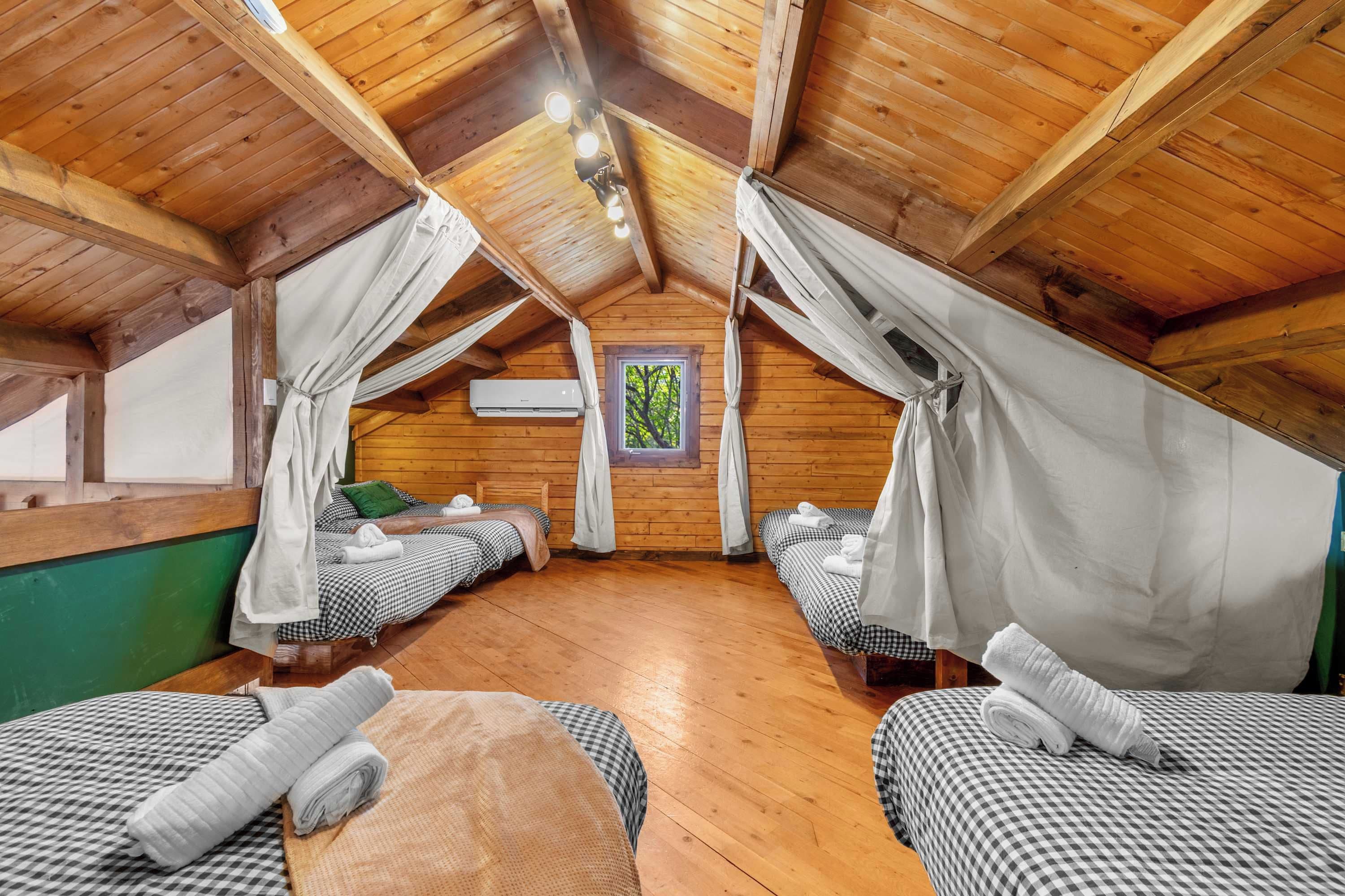 A cozy attic bedroom with two beds, wooden beams, and a view of greenery outside.