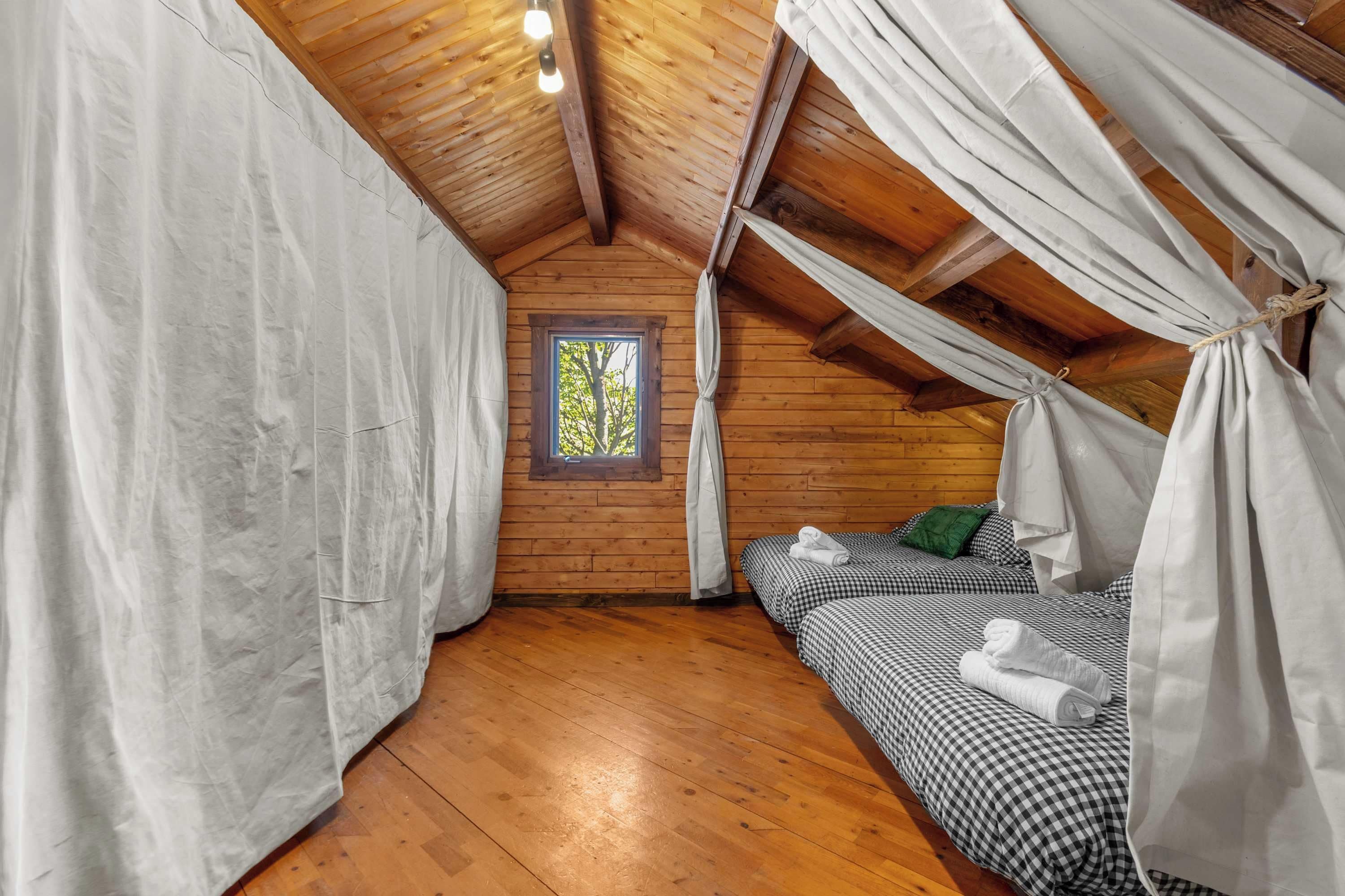 A cozy attic bedroom with a wooden ceiling, a small window, and a bed with checkered bedding.