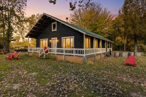 Une cabane avec une véranda, un escalier et deux chaises Adirondack rouges.