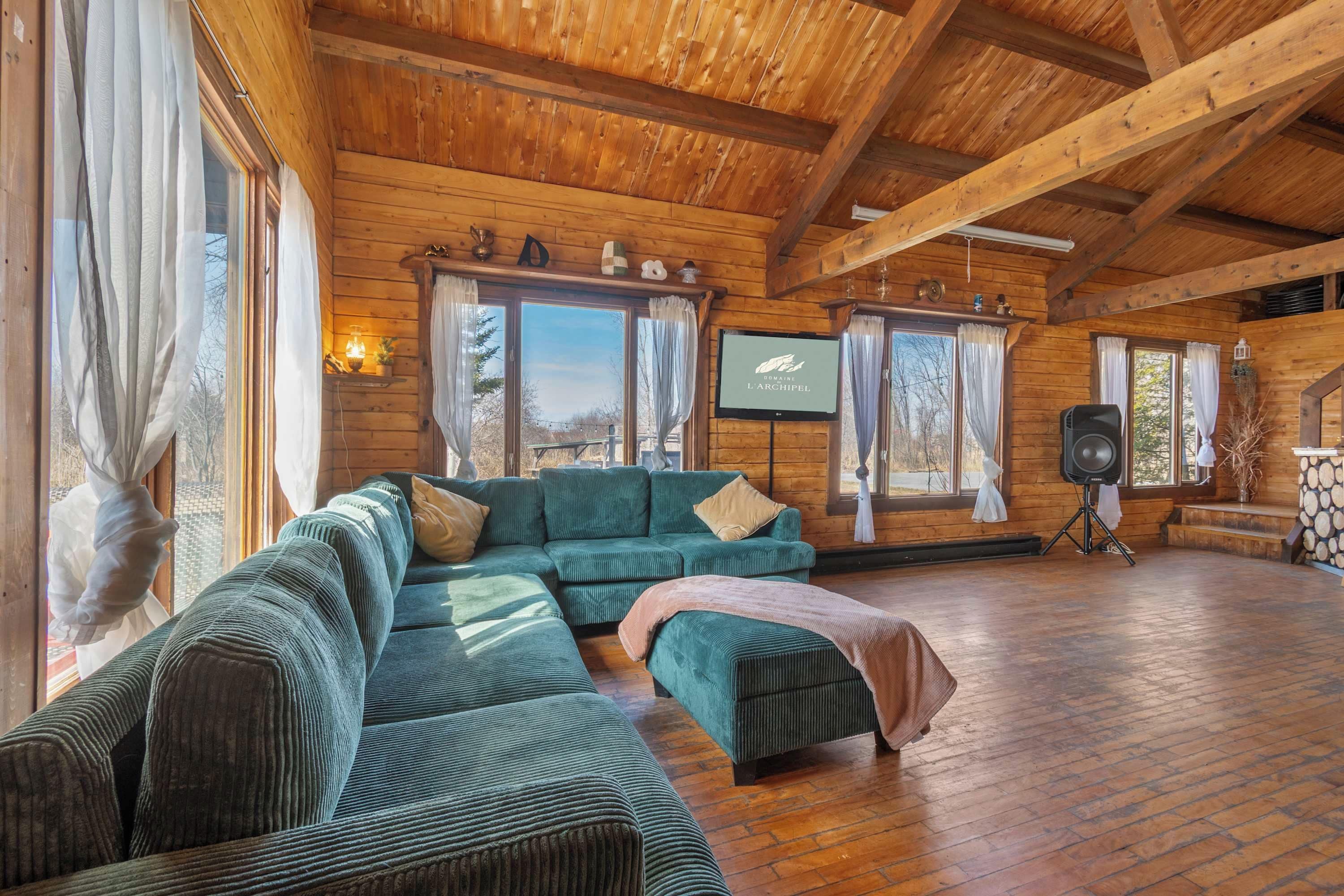 Ein Innenraum einer Blockhütte mit einem Ecksofa, einem Fernseher und einem Kamin.