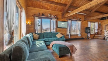 Ein Innenraum einer Blockhütte mit einem Ecksofa, einem Fernseher und einem Kamin.