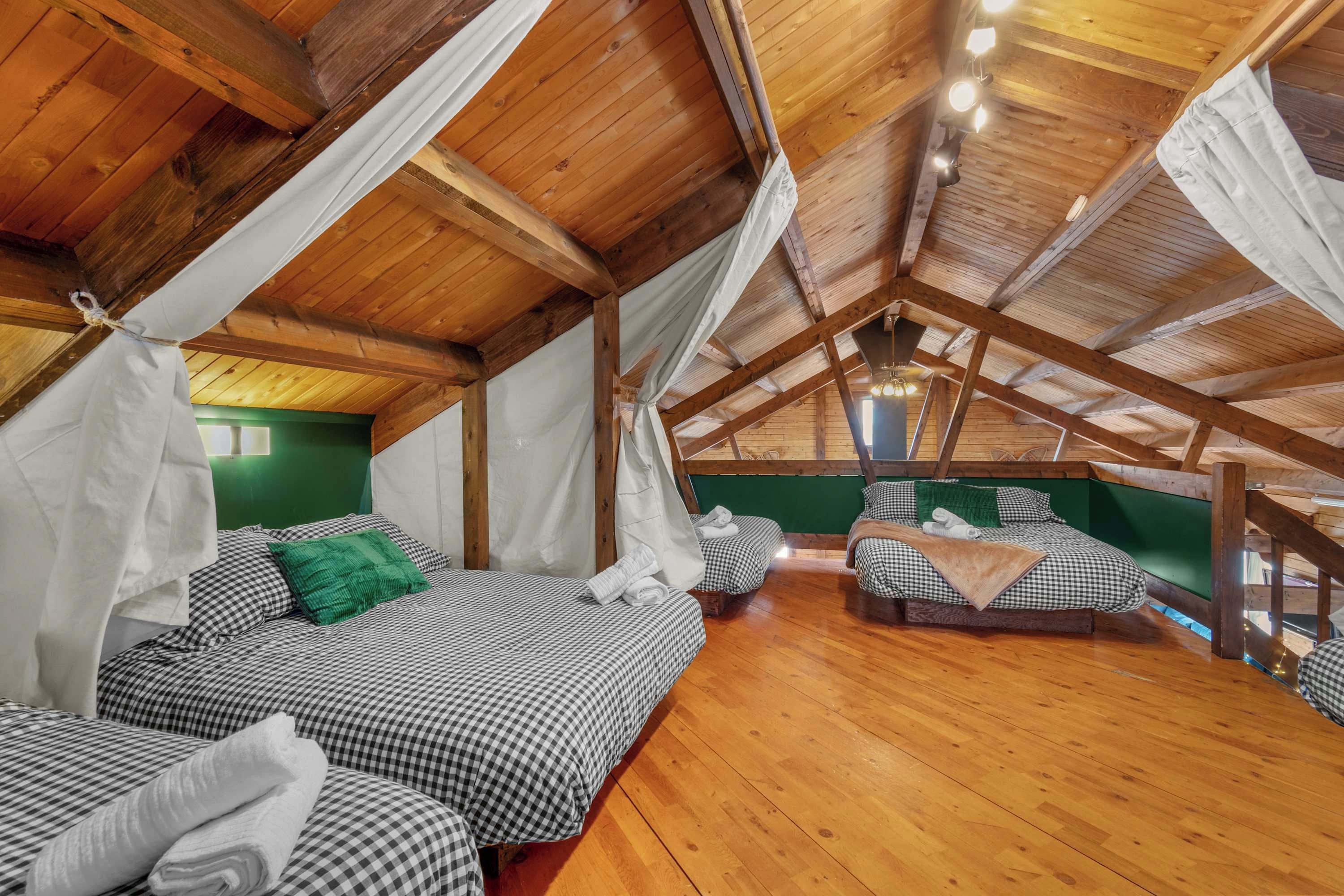 A high-ceilinged room with wooden beams, checkered bedding, and a green accent wall.