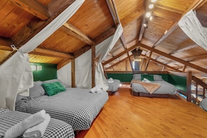 Une pièce aux hauts plafonds, avec des poutres en bois, une literie à carreaux et un mur d’accent vert.