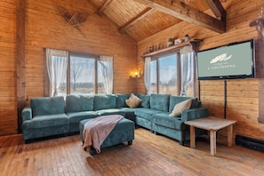 A cozy cabin interior with a sectional sofa, a small table, and a television mounted on the wall.