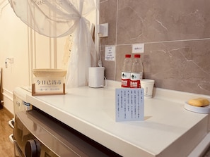 A hotel room counter with a white basin, a mosquito net, a white cup, two water bottles, and a sign indicating free water. - Cloudwards City Homestay Zhengzhou (Zhengzhou)
