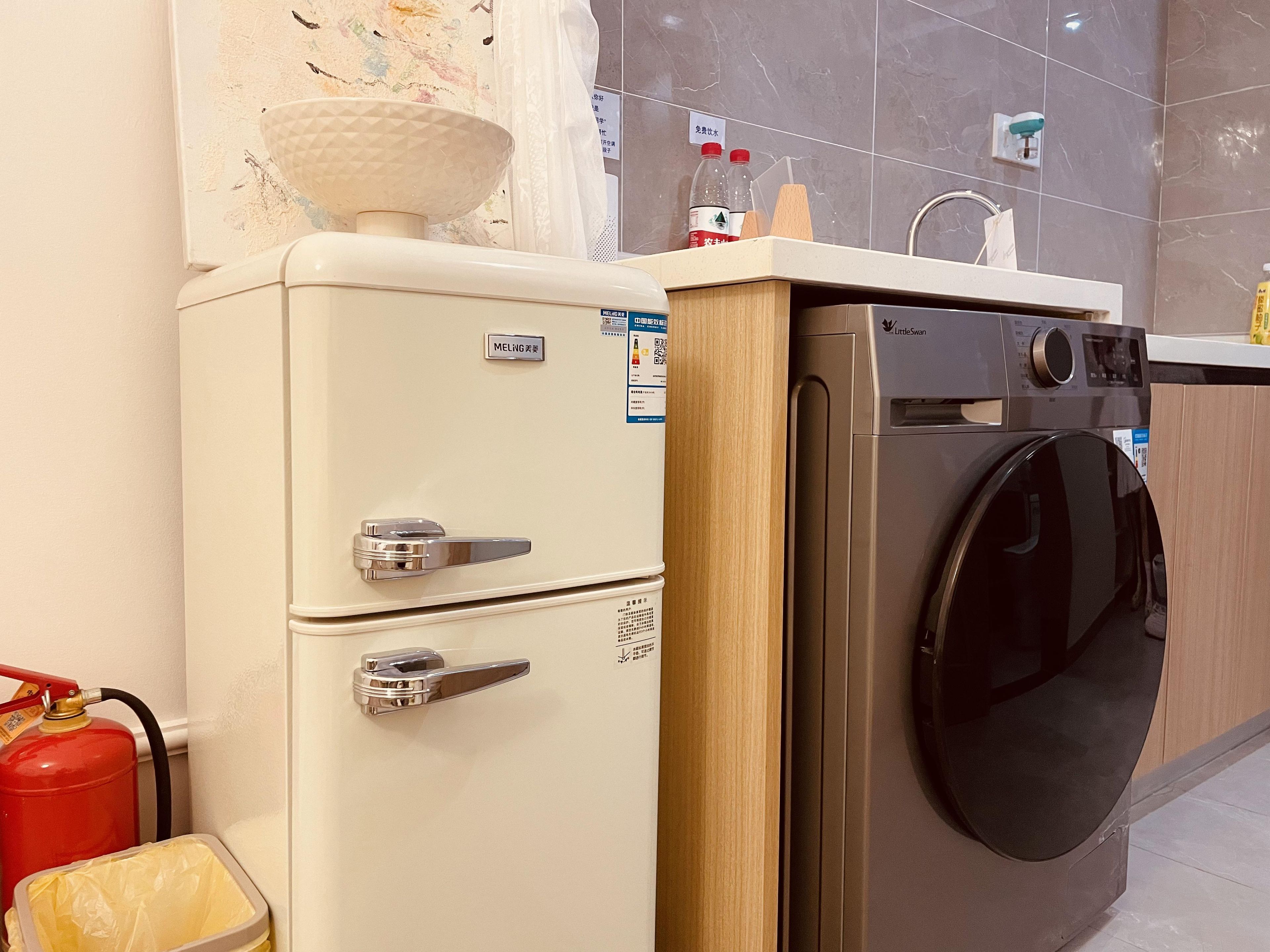 Una kitchenette compacta con un refrigerador de estilo vintage, una lavadora moderna y un extintor.