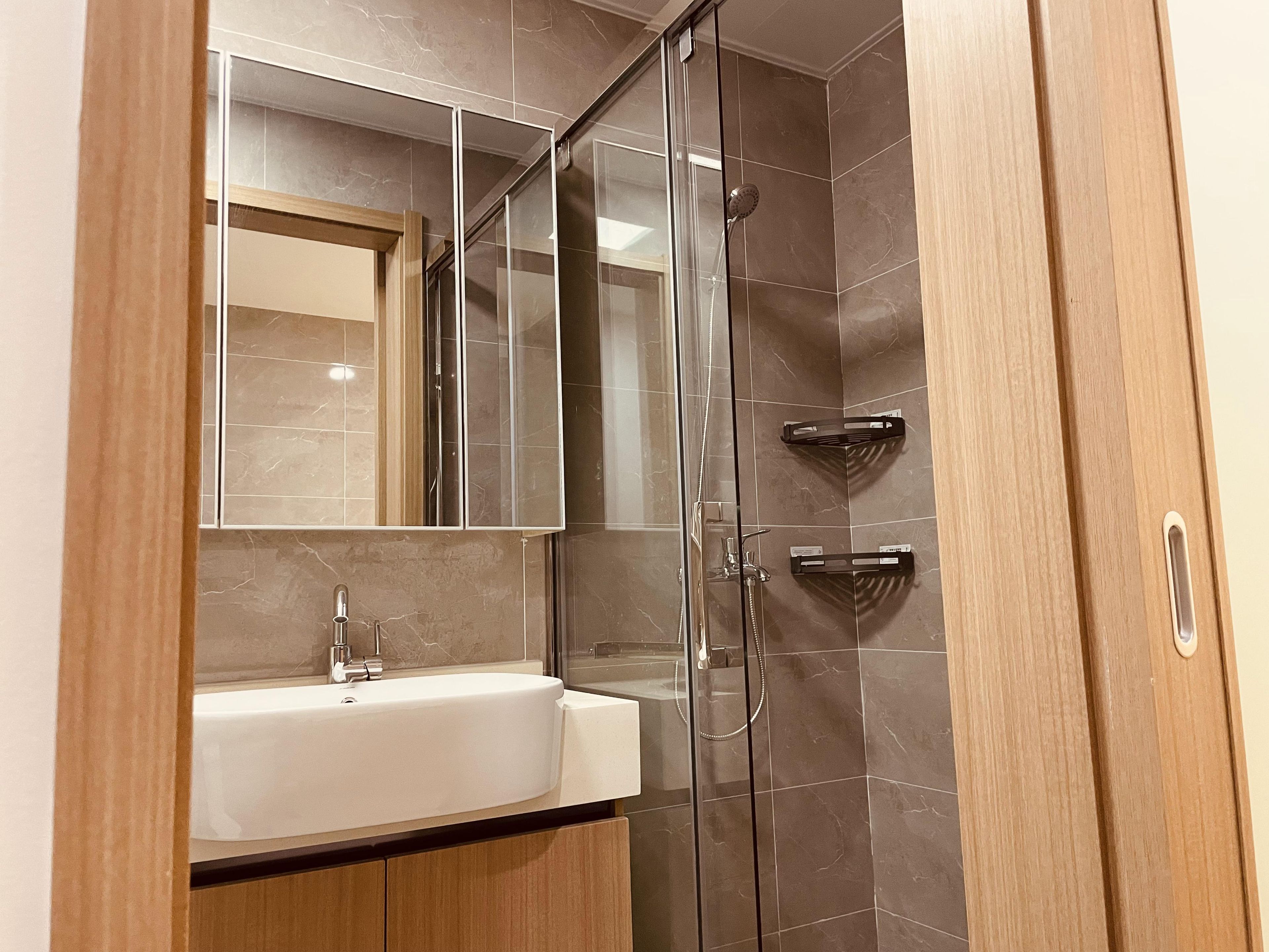 A modern bathroom with a glass shower enclosure, a white sink, and a wooden vanity.