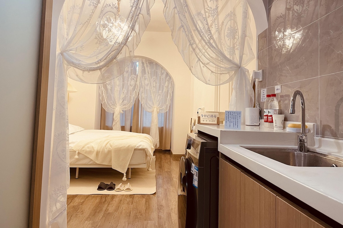 A hotel room with a bed, a bathroom with a sink, and a washing machine.