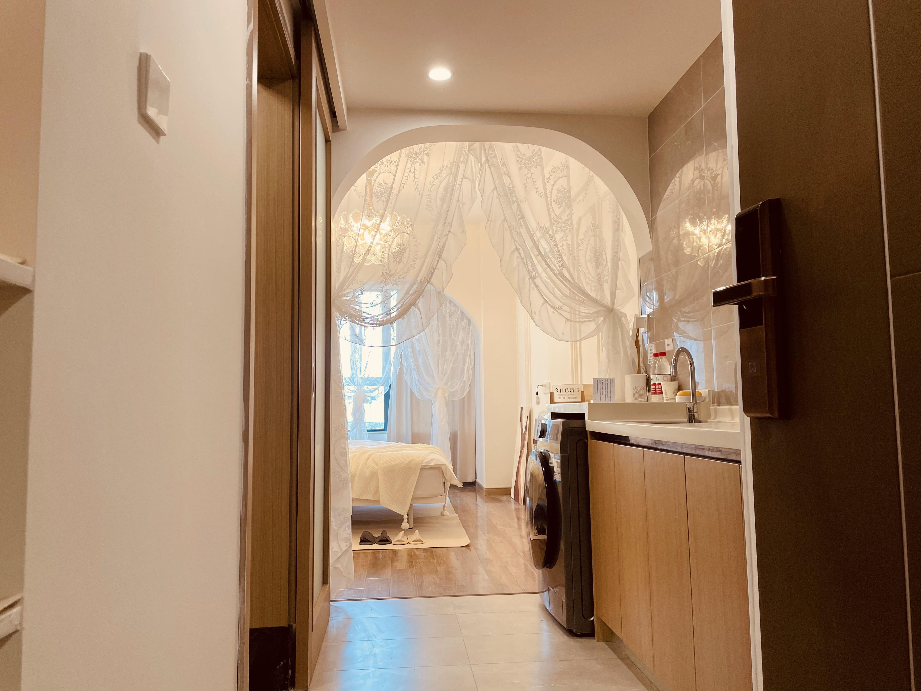 A hallway leading to a bedroom with a bed, a washing machine, and a sink.