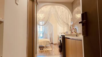 A hallway leading to a bedroom with a bed, a washing machine, and a sink.