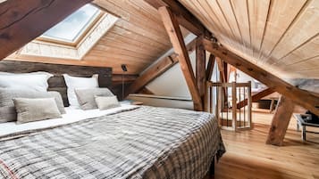 A loft bedroom with a sloped ceiling, wooden beams, a skylight, a bed with a patterned bedspread, and a bedside table.