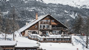 A chalet-style hotel with a ski lift in the background, surrounded by snow-covered mountains.