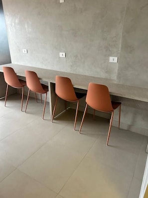 A row of four orange chairs with metal legs, aligned against a wall with a textured surface. - Amazing View in Downtown | Peace and Quiet, Style, and Fast Internet (Curitiba)