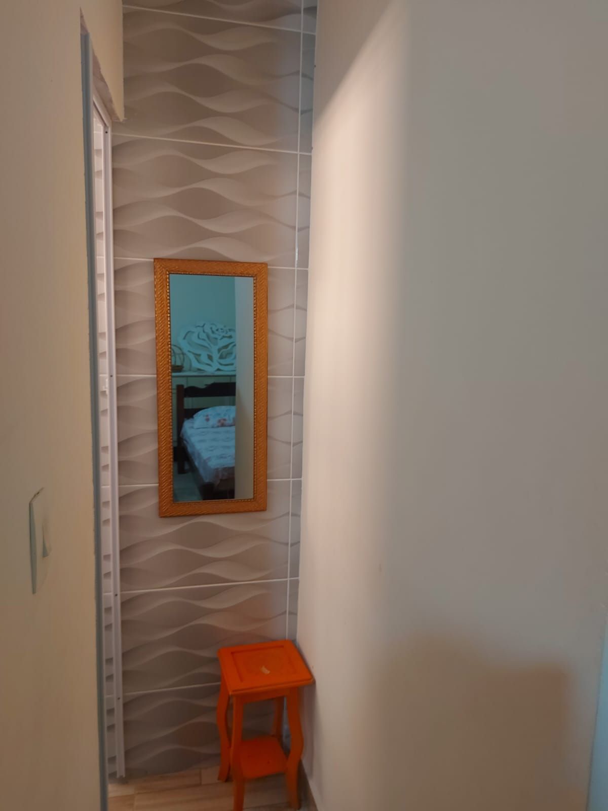 Un couloir étroit avec un mur à texture, un miroir et un petit tabouret en bois.