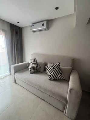 A modern living room with a beige sofa, two patterned pillows, a ceiling-mounted air conditioner, and a large window with curtains. - Marrakech, Guéliz, Dar Mekki (Marrakech)