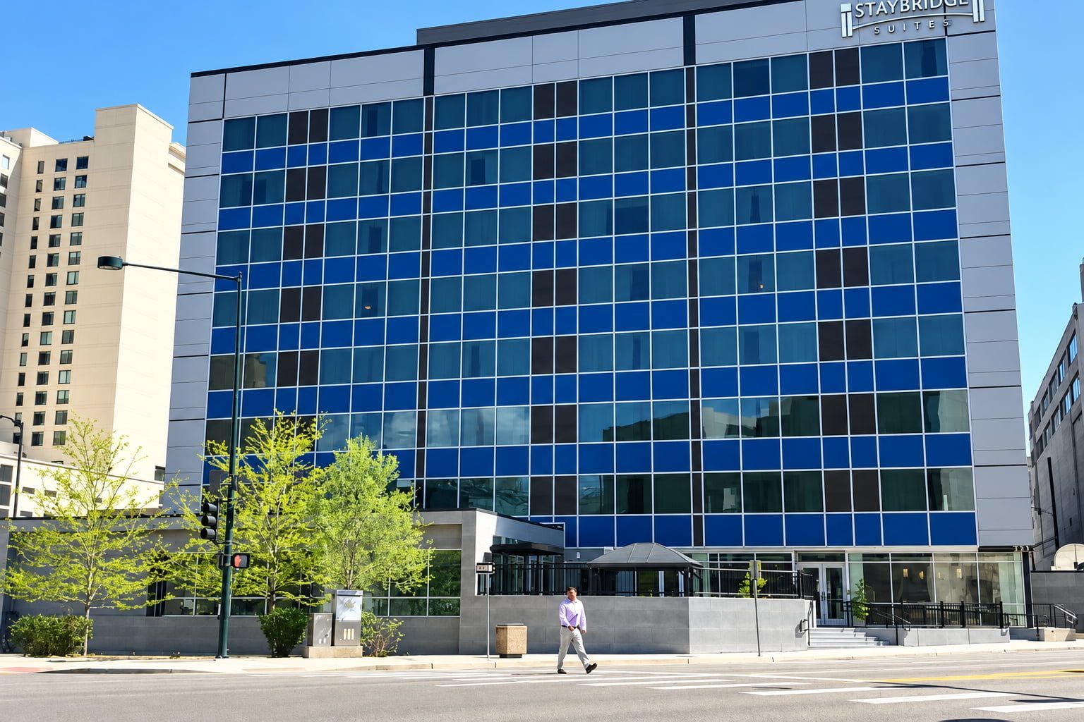 Un bâtiment d’hôtel moderne avec une façade en verre, une enseigne indiquant « Staybridge Suites » et un passage piéton.