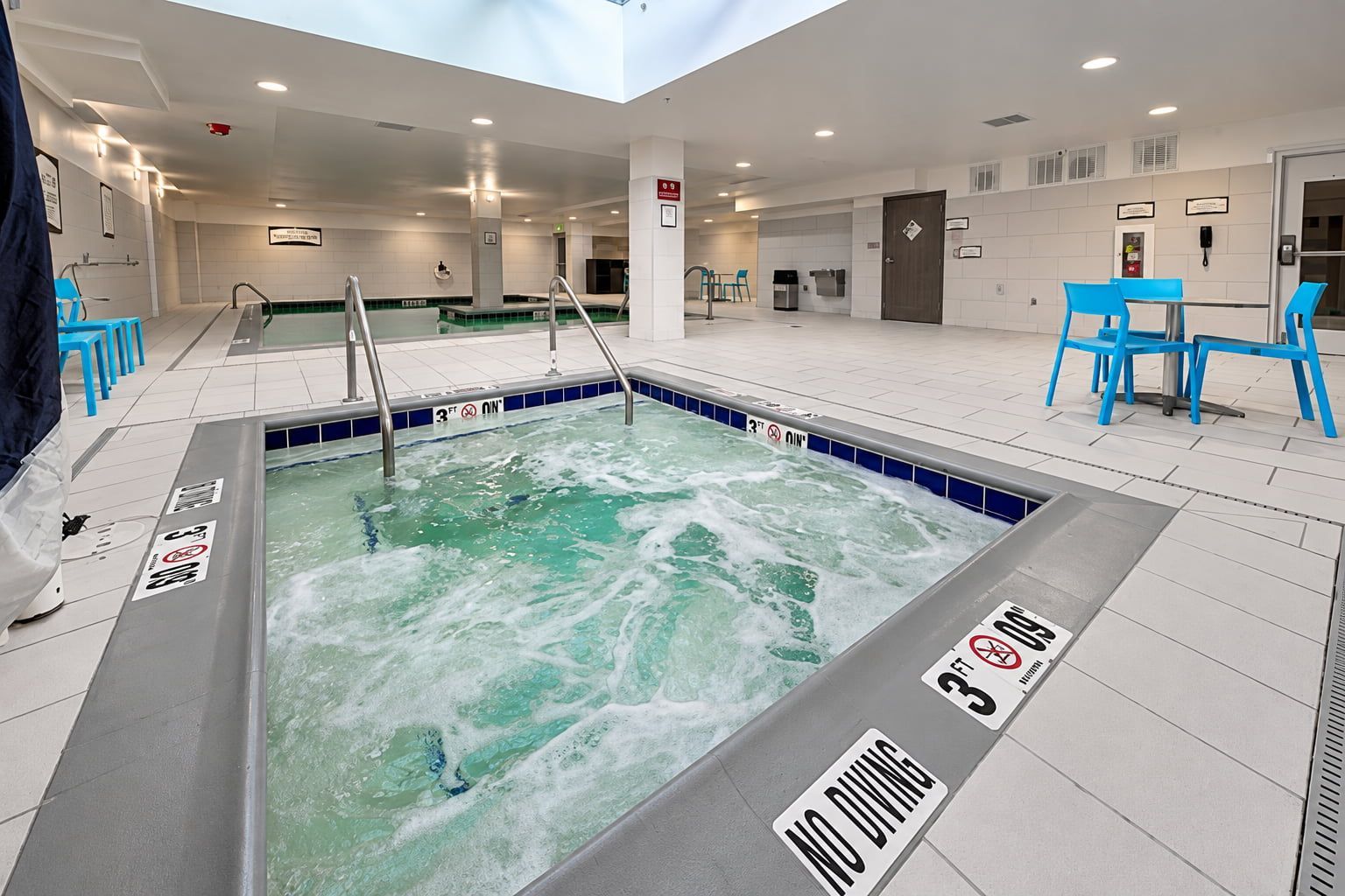A hot tub with a 'NO DIVING' sign, surrounded by blue chairs and a tiled floor.