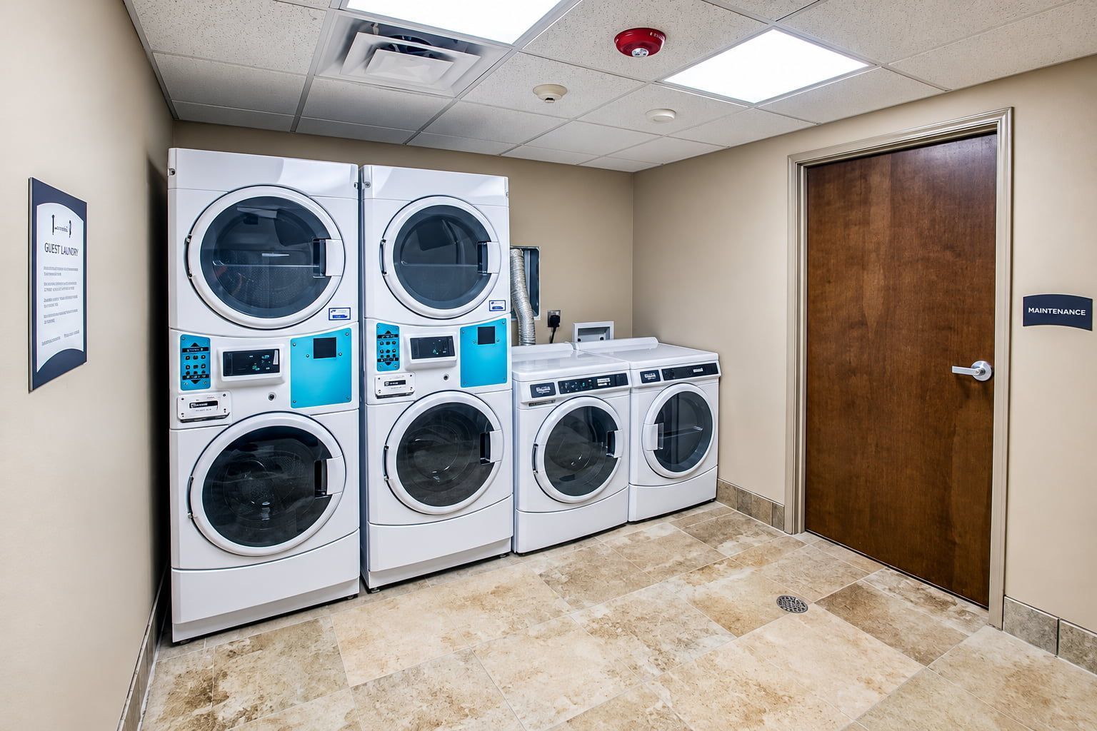 A laundry facility with four stacked washing machines, a maintenance door, and a sign indicating guest laundry services.