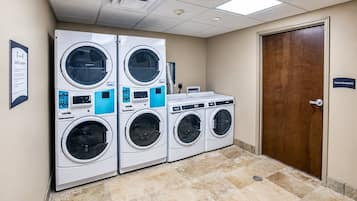 A laundry facility with four stacked washing machines, a maintenance door, and a sign indicating guest laundry services.