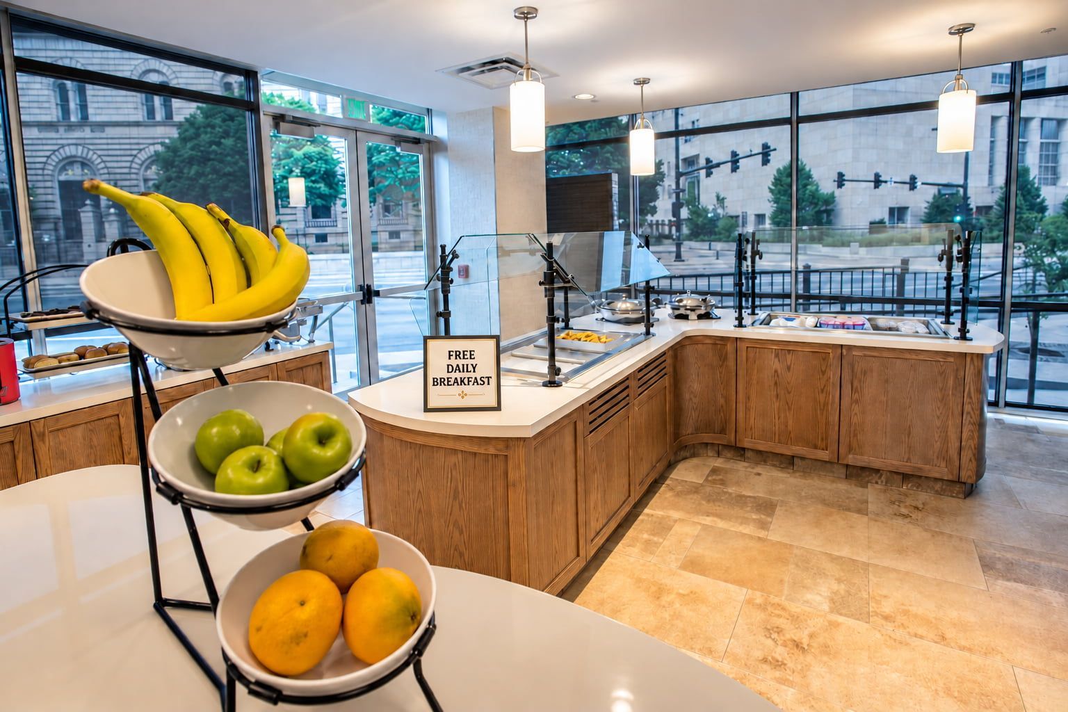 A modern kitchen with a breakfast bar, fruit bowls, and a sign offering free daily breakfast.