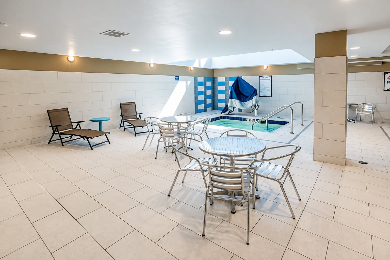 A pool area with lounge chairs and tables, a tiled floor, and a blue and white wall pattern.