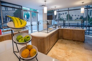 Une cuisine avec un panier de fruits contenant des bananes, des pommes et des oranges, un évier et des armoires en bois.