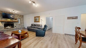 A living room with a stone fireplace, leather sofa, and a dining area with wooden furniture. - Renovated Mountain Apartment, Private Entrance, Seasonal Mountain Views, Covered Porch, Air Conditioning (Waynesville)