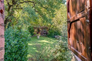 Eine rustikale Holzhütte in einem üppigen Garten mit einer Steinmauer und einer Holztür.