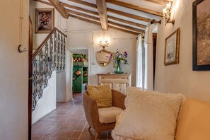 Ein Flur mit einer Holztreppe, einem Korbsessel, einem weißen Sofa und einem Spiegel an der Wand.
