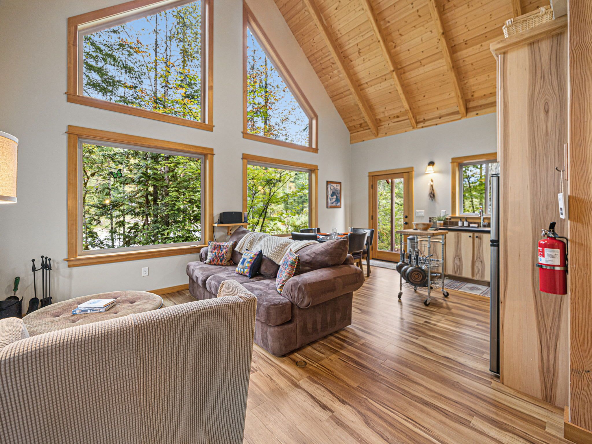 A spacious living room with a large couch, a dining area, and a kitchen with wooden flooring and large windows.